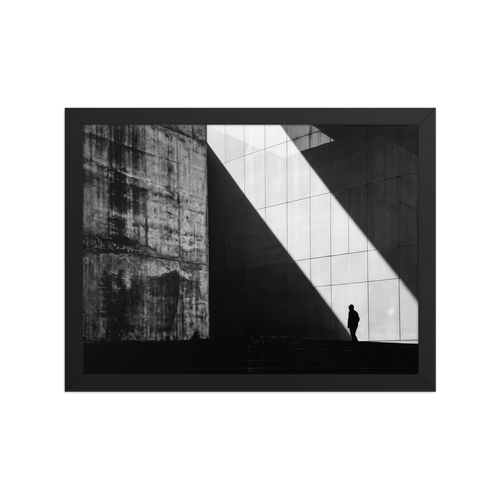 'Urban Geometry' — a Modernism print. A high-contrast black and white architectural photograph featuring a sharp diagonal shaft of light and a lone silhouette walking past textured concrete walls, perfect for an Office or Modern Living Room.