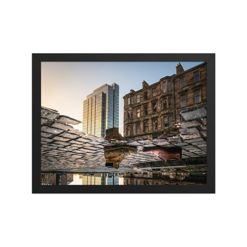 'Steps Through Time' — a Art photography print. Creative puddle reflection photograph showing a work boot and a dress shoe on cobblestones, with a modern glass skyscraper and an old stone building in the background, ideal for an office or hallway.