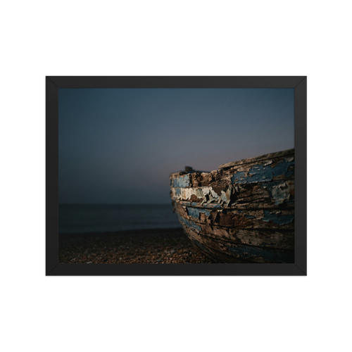 'The Faded Blue Boat' — a Art photography print. Close-up photograph of a weathered wooden boat with peeling blue paint resting on a rocky beach at dusk, suitable for a serene bathroom or living room.