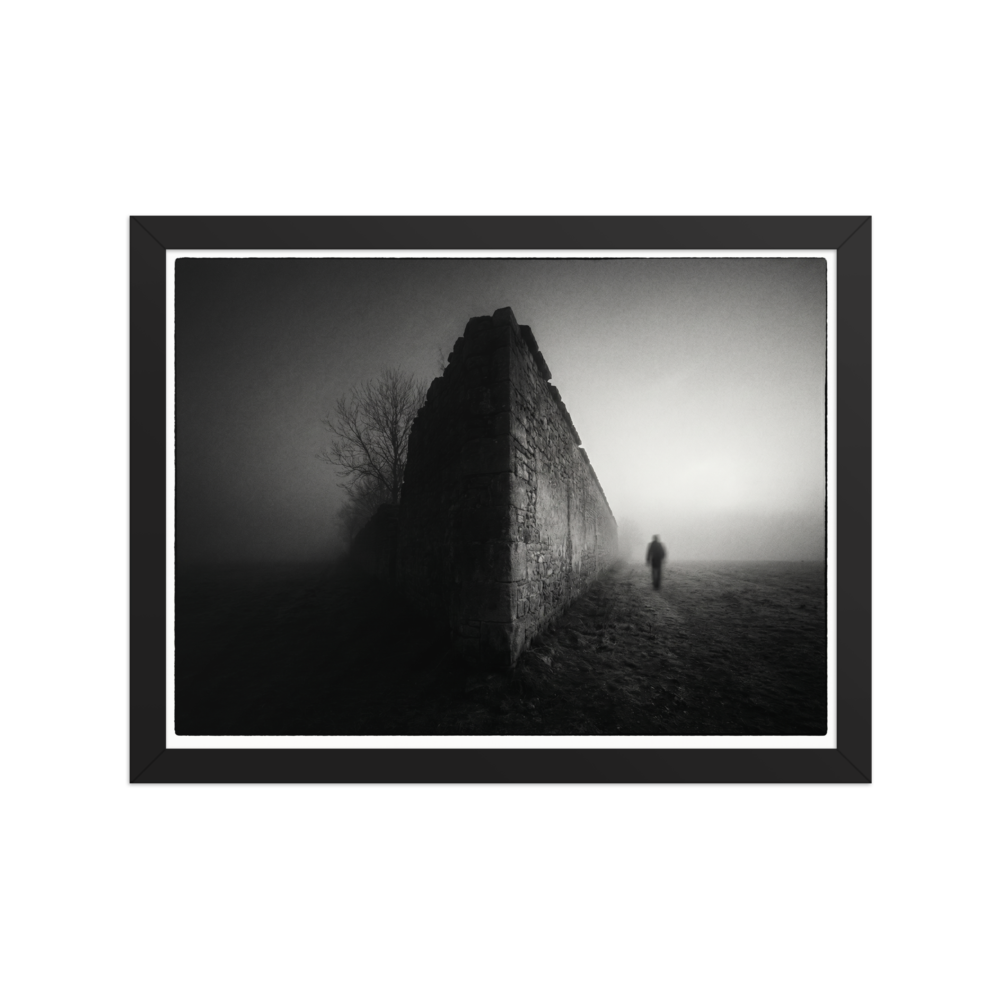 'Echoes in the Mist' — a Art photography print. A moody black and white photograph of a lone figure walking into dense fog next to an old stone wall, ideal for a modern Office or Den.