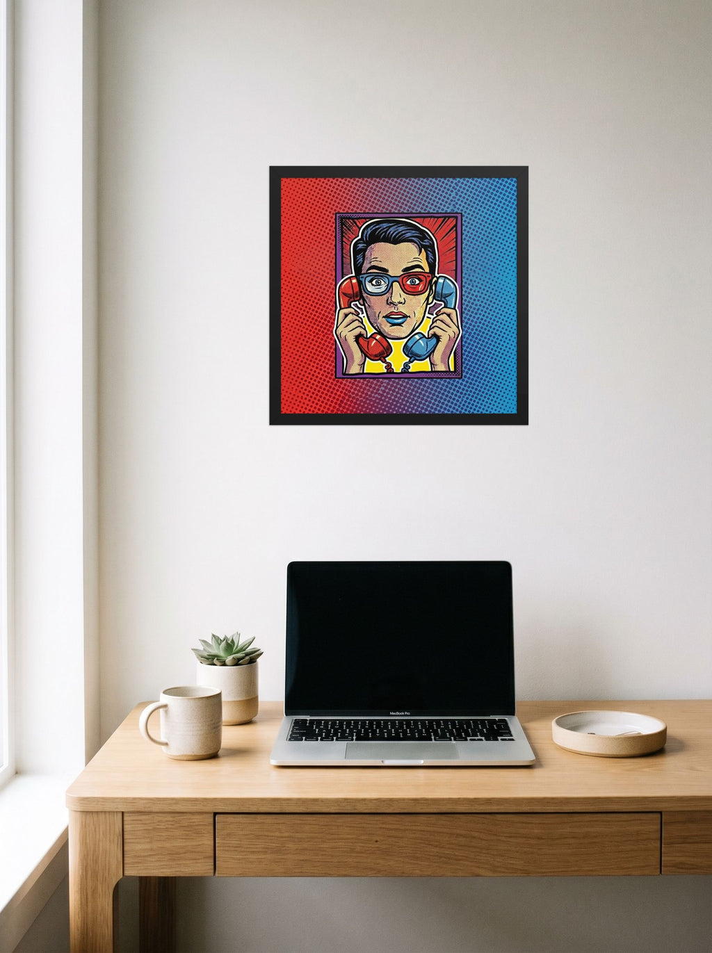 A 16x16 inch black framed Pop art print of 'Bipartisan Static' hanging above a worktable with a laptop.