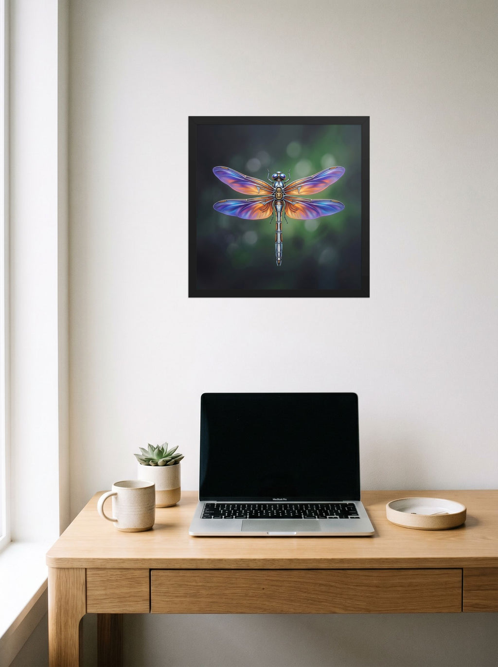 A 16x16 inch black framed Surrealism print of 'Gears of the Dragonfly' hanging above a worktable with a laptop.