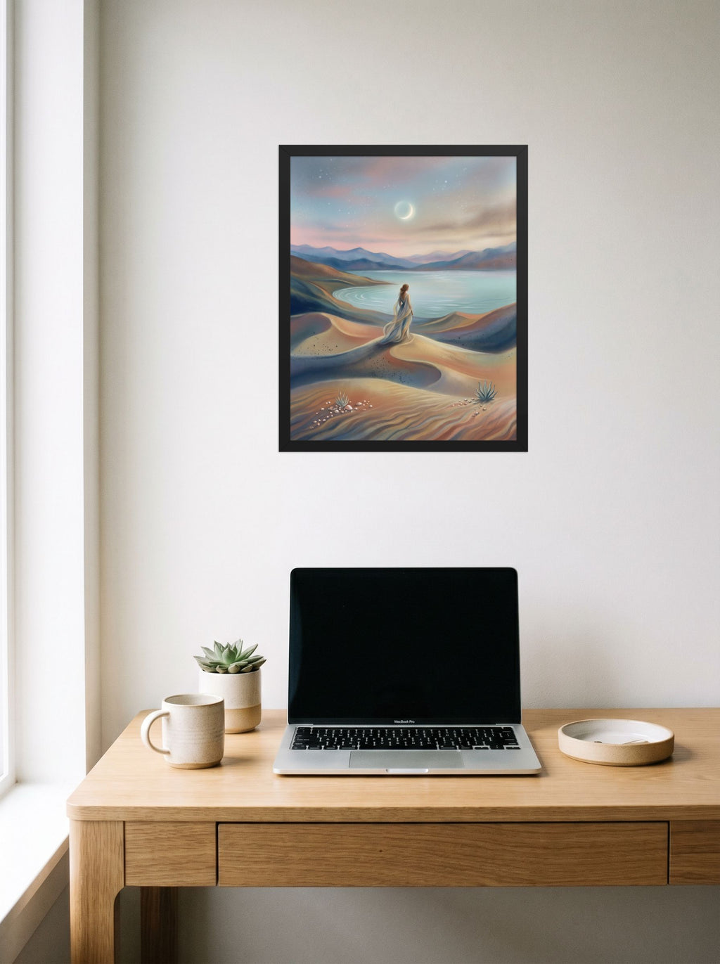 A 16x20 inch black framed Magic realism print of 'Desert Moonrise' hanging above a worktable with a laptop.