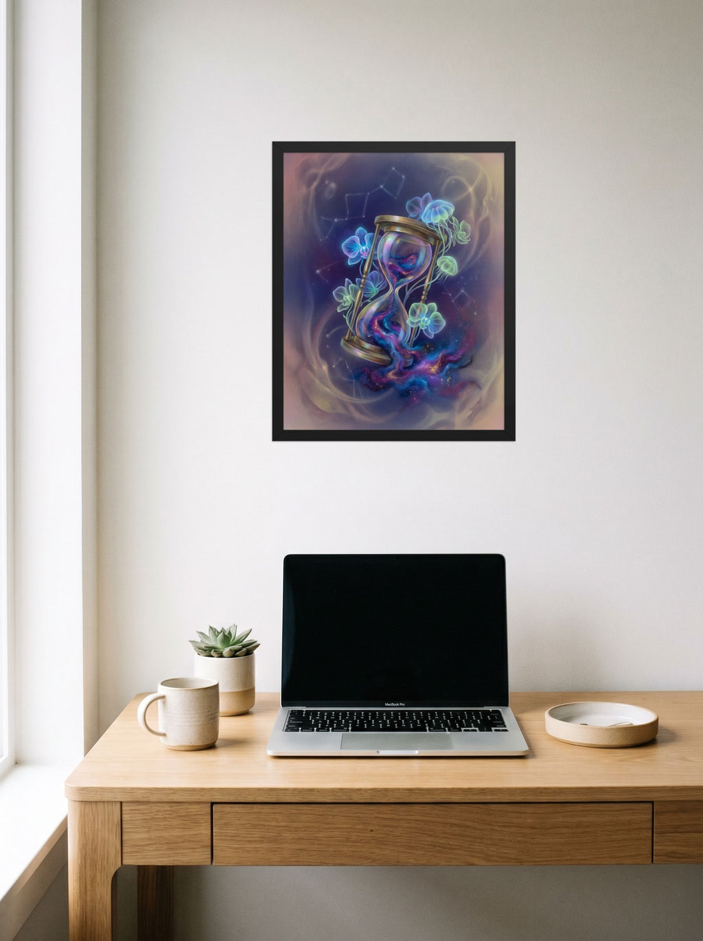 A 16x20 inch black framed Magic realism print of 'Sands of the Nebula' hanging above a worktable with a laptop.