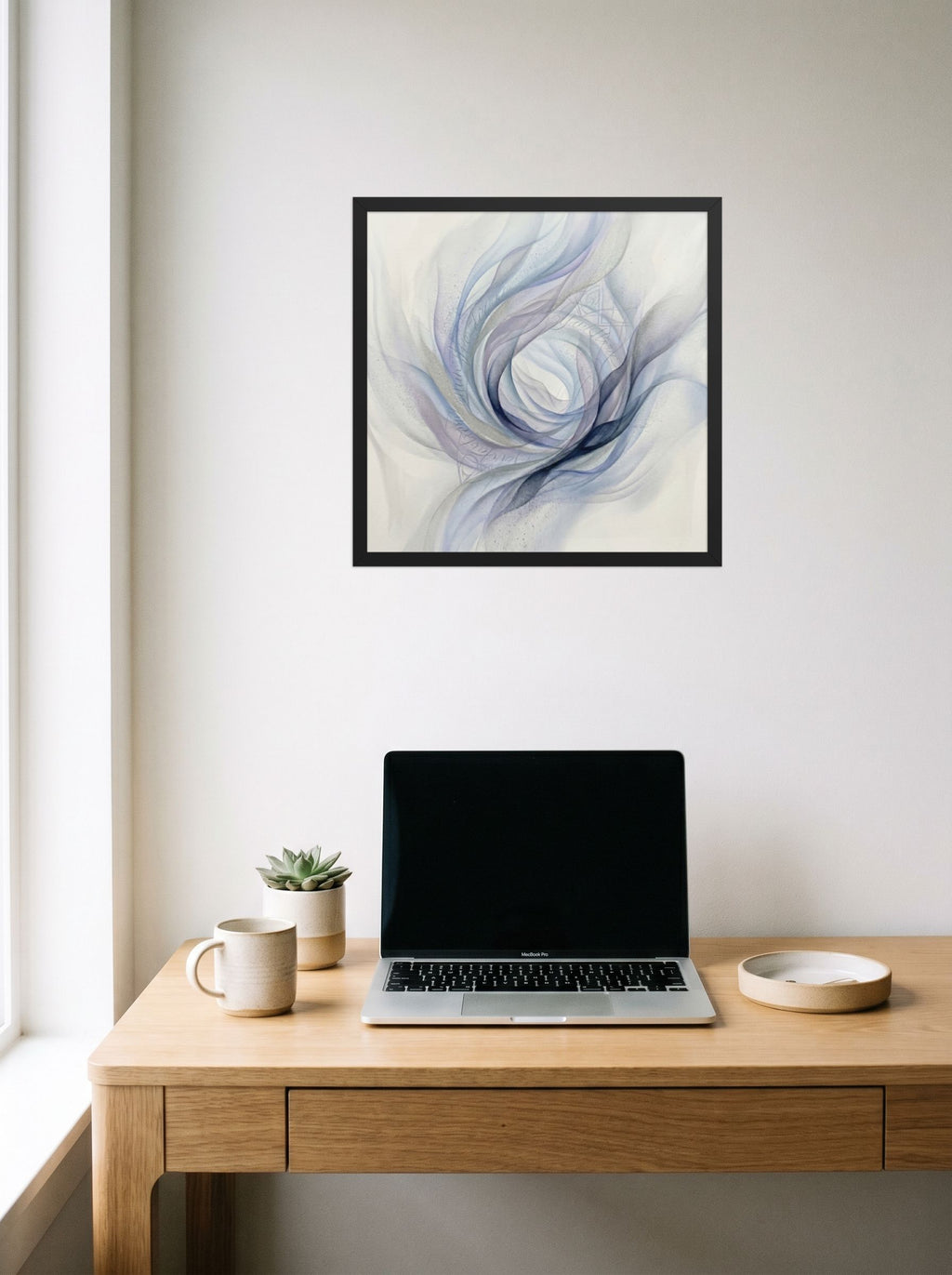 A 18x18 inch black framed Abstract art print of 'Ethereal Whispers in the Vortex' hanging above a worktable with a laptop.
