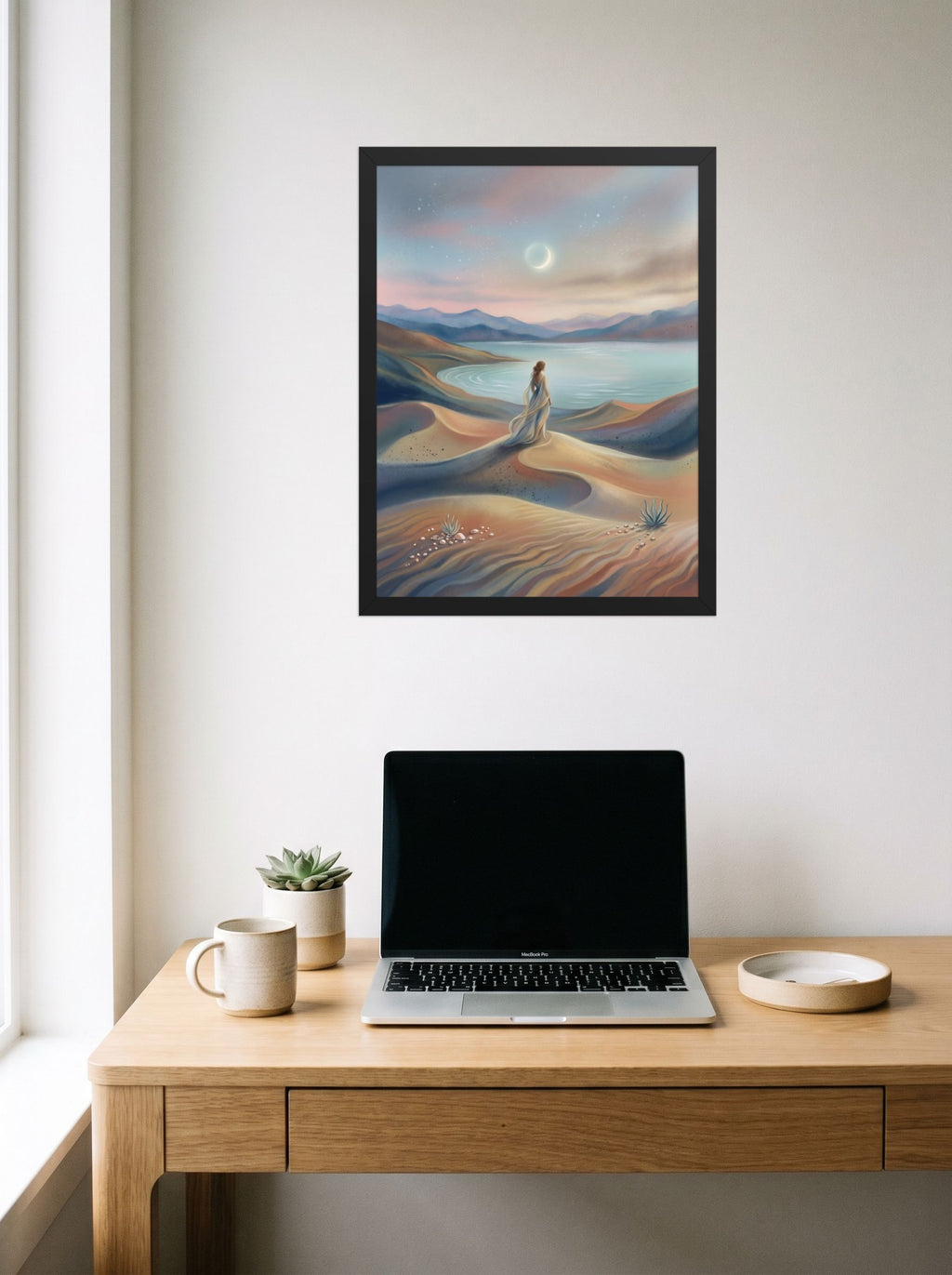 A 18x24 inch black framed Magic realism print of 'Desert Moonrise' hanging above a worktable with a laptop.