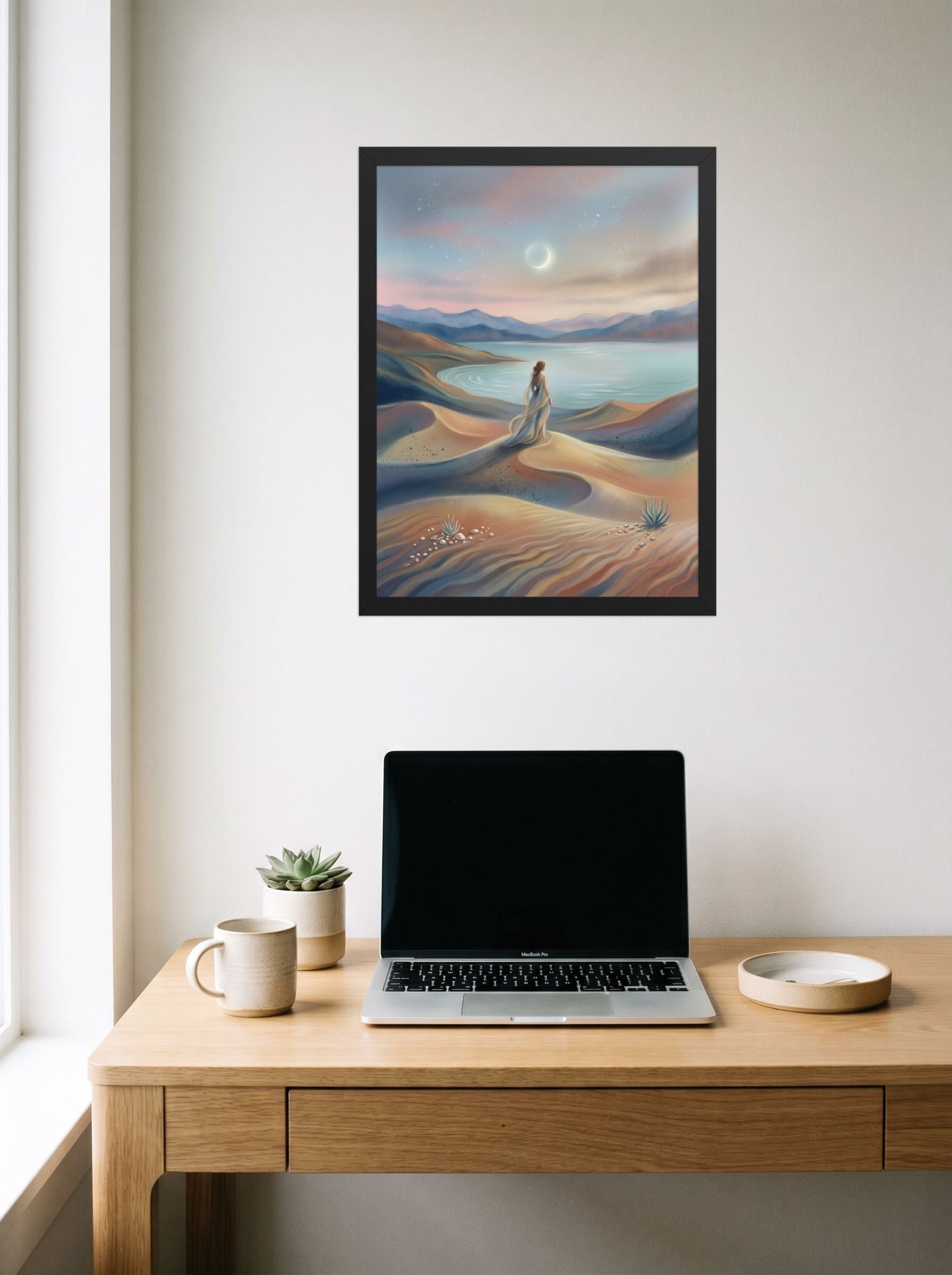 A 18x24 inch black framed Magic realism print of 'Desert Moonrise' hanging above a worktable with a laptop.