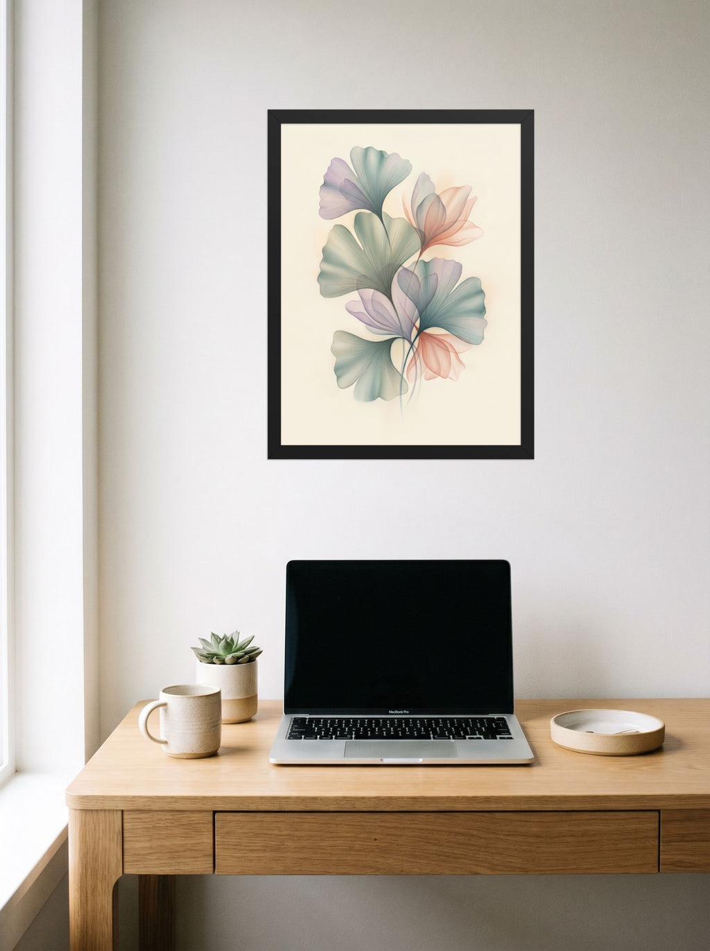 A 18x24 inch black framed Abstract art print of 'Ethereal Ginkgo Whispers' hanging above a worktable with a laptop.