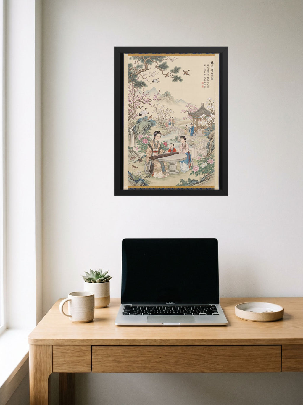 A 18x24 inch black framed Fine Art print of 'Melody in the Spring Garden' hanging above a worktable with a laptop.