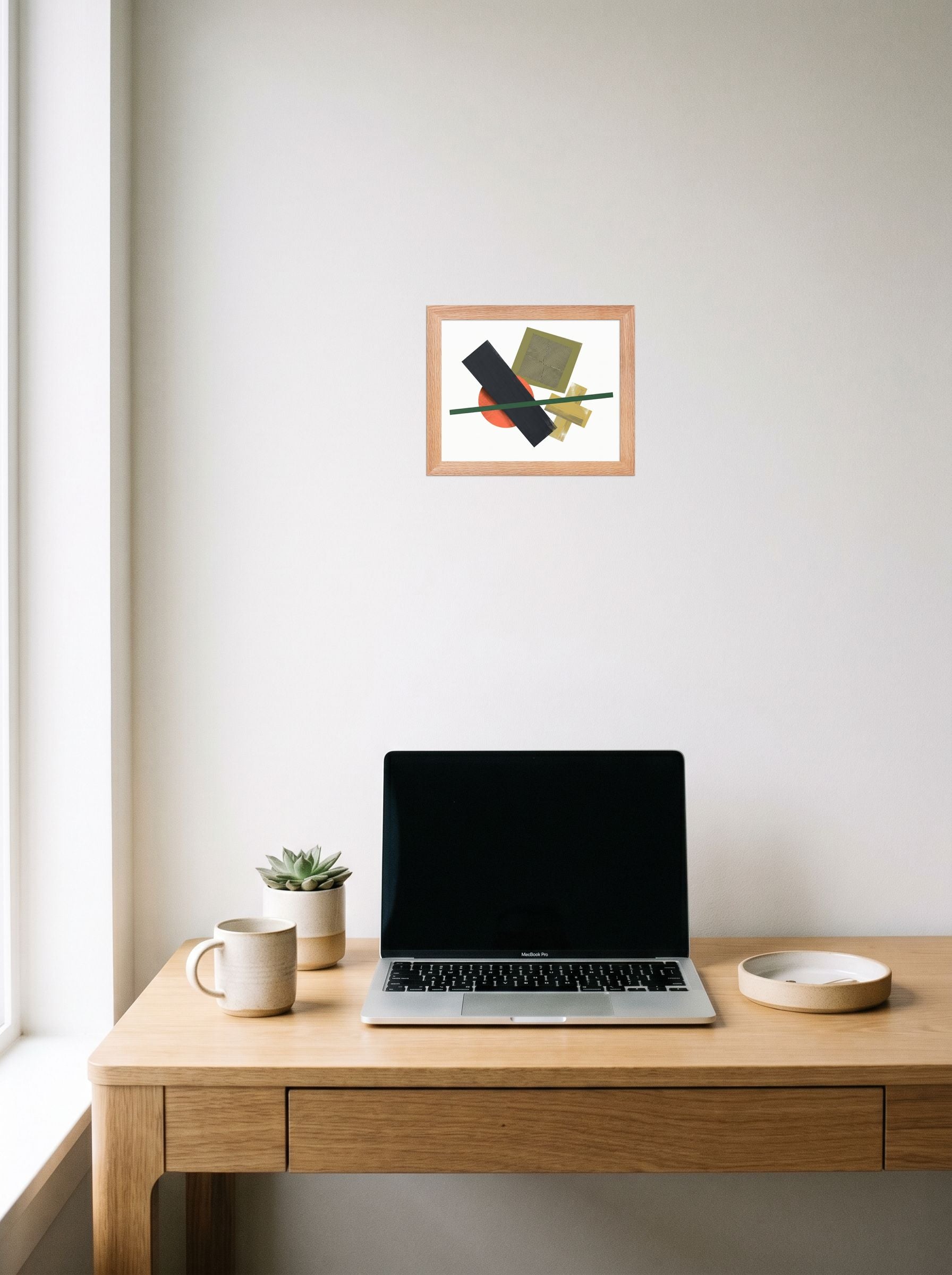 A 10x8 inch redoak framed Suprematism print of 'The Geometry of Sound' hanging above a worktable with a laptop.