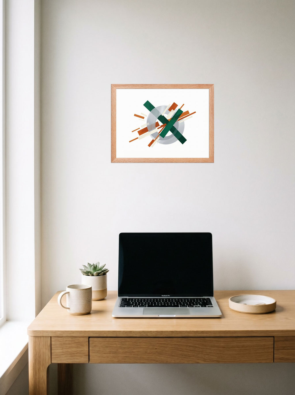 A 16x12 inch redoak framed Suprematism print of 'Intersecting Perspectives' hanging above a worktable with a laptop.