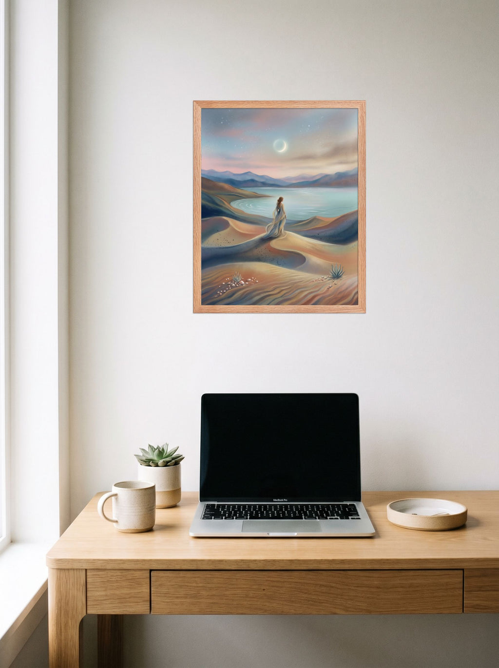 A 16x20 inch redoak framed Magic realism print of 'Desert Moonrise' hanging above a worktable with a laptop.