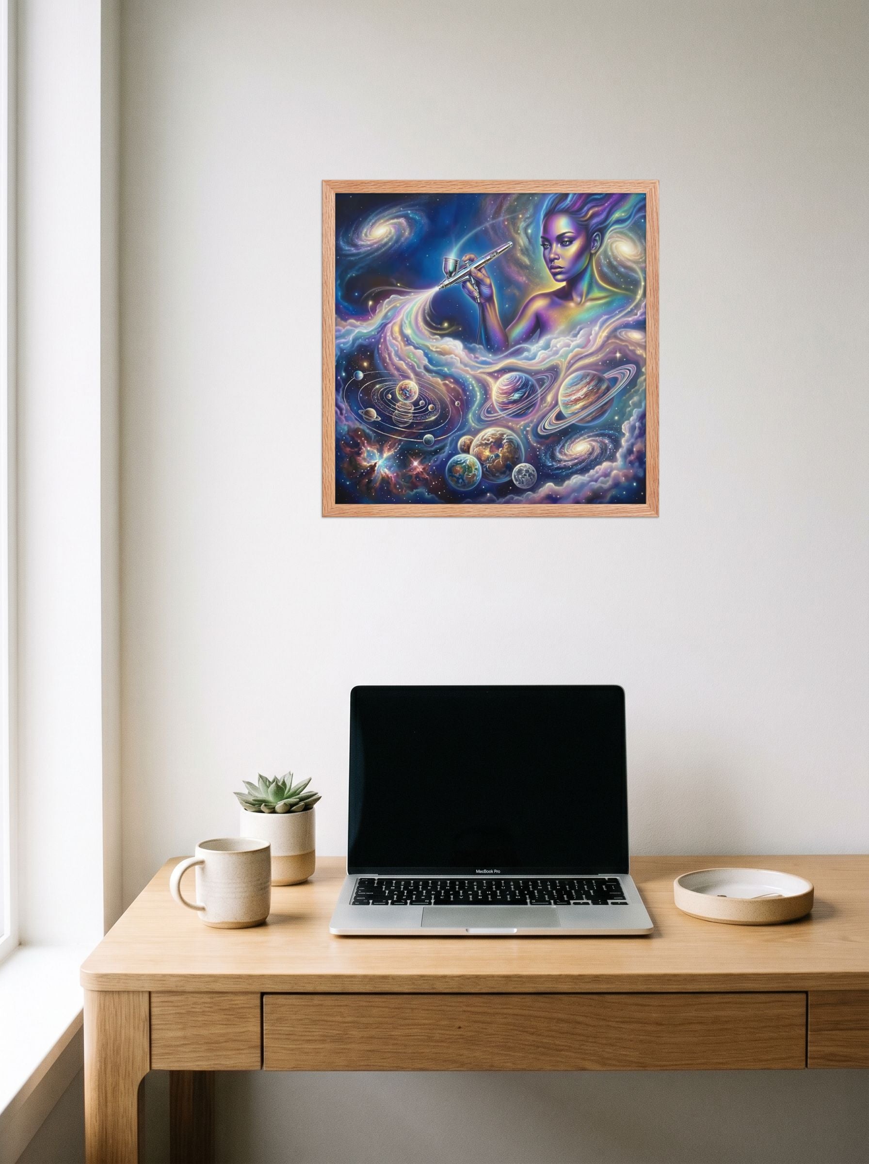 A 18x18 inch redoak framed Space art print of 'The Cosmic Painter' hanging above a worktable with a laptop.
