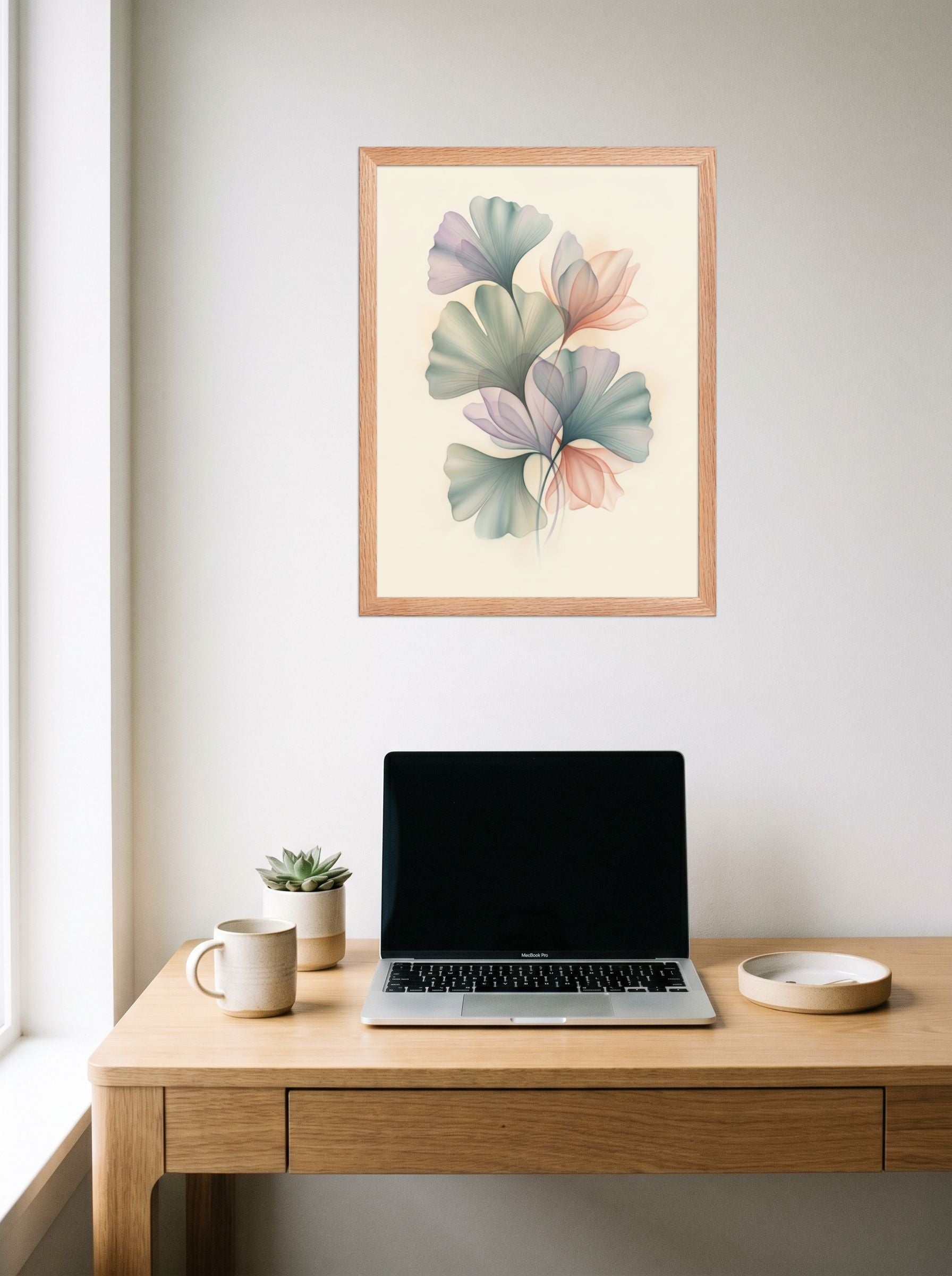 A 18x24 inch redoak framed Abstract art print of 'Ethereal Ginkgo Whispers' hanging above a worktable with a laptop.