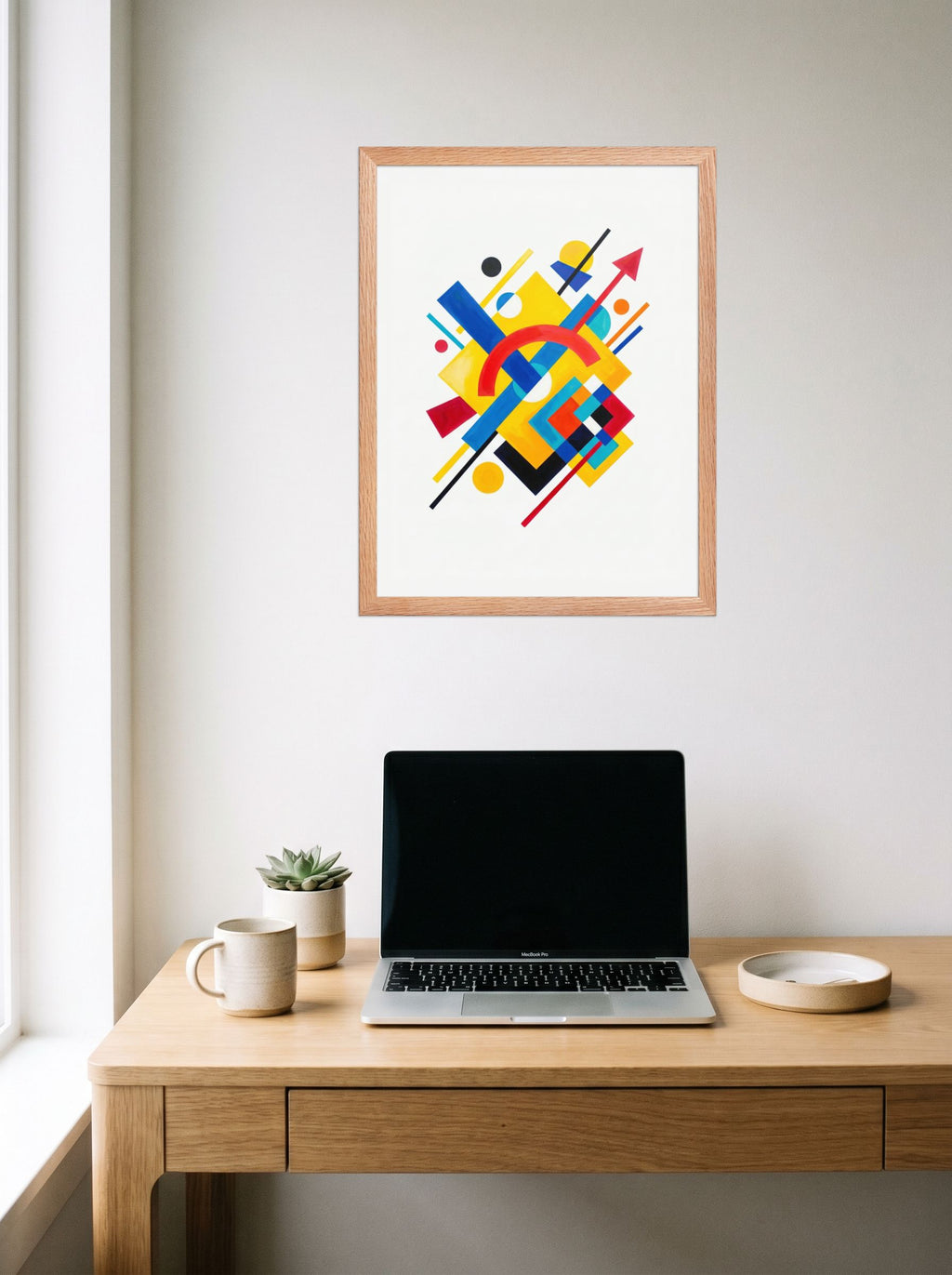 A 18x24 inch redoak framed Suprematism print of 'Directional Energy' hanging above a worktable with a laptop.
