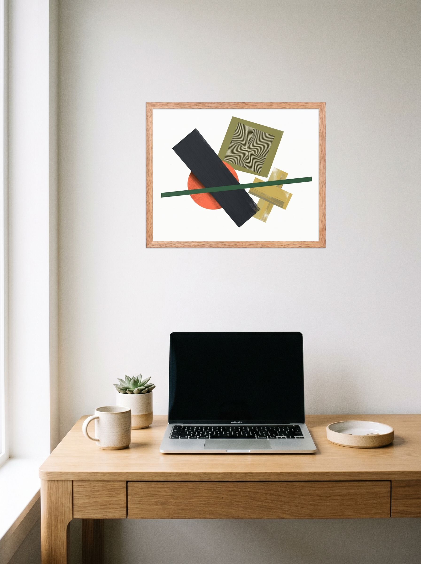 A 20x16 inch redoak framed Suprematism print of 'The Geometry of Sound' hanging above a worktable with a laptop.