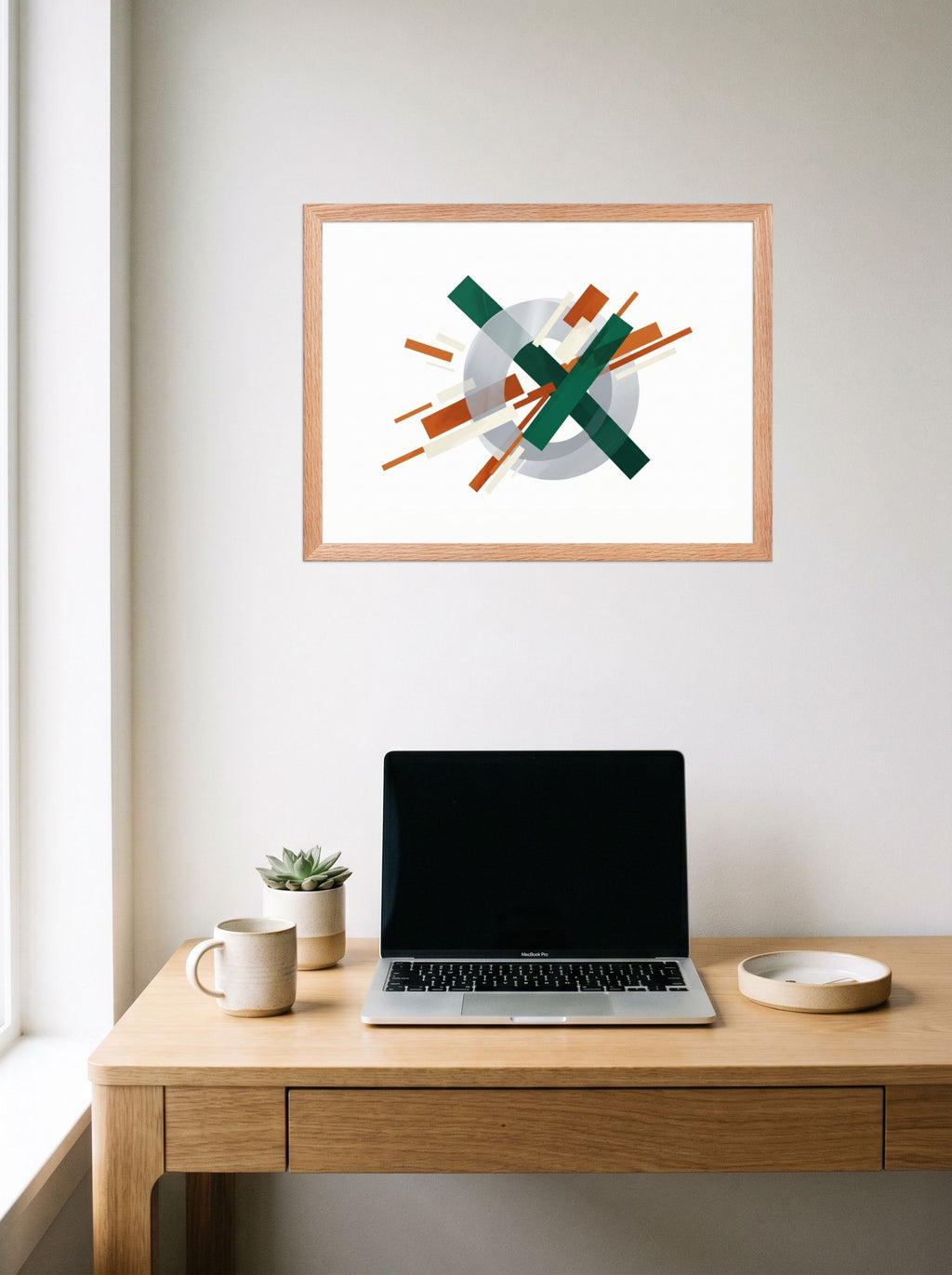 A 24x18 inch redoak framed Suprematism print of 'Intersecting Perspectives' hanging above a worktable with a laptop.