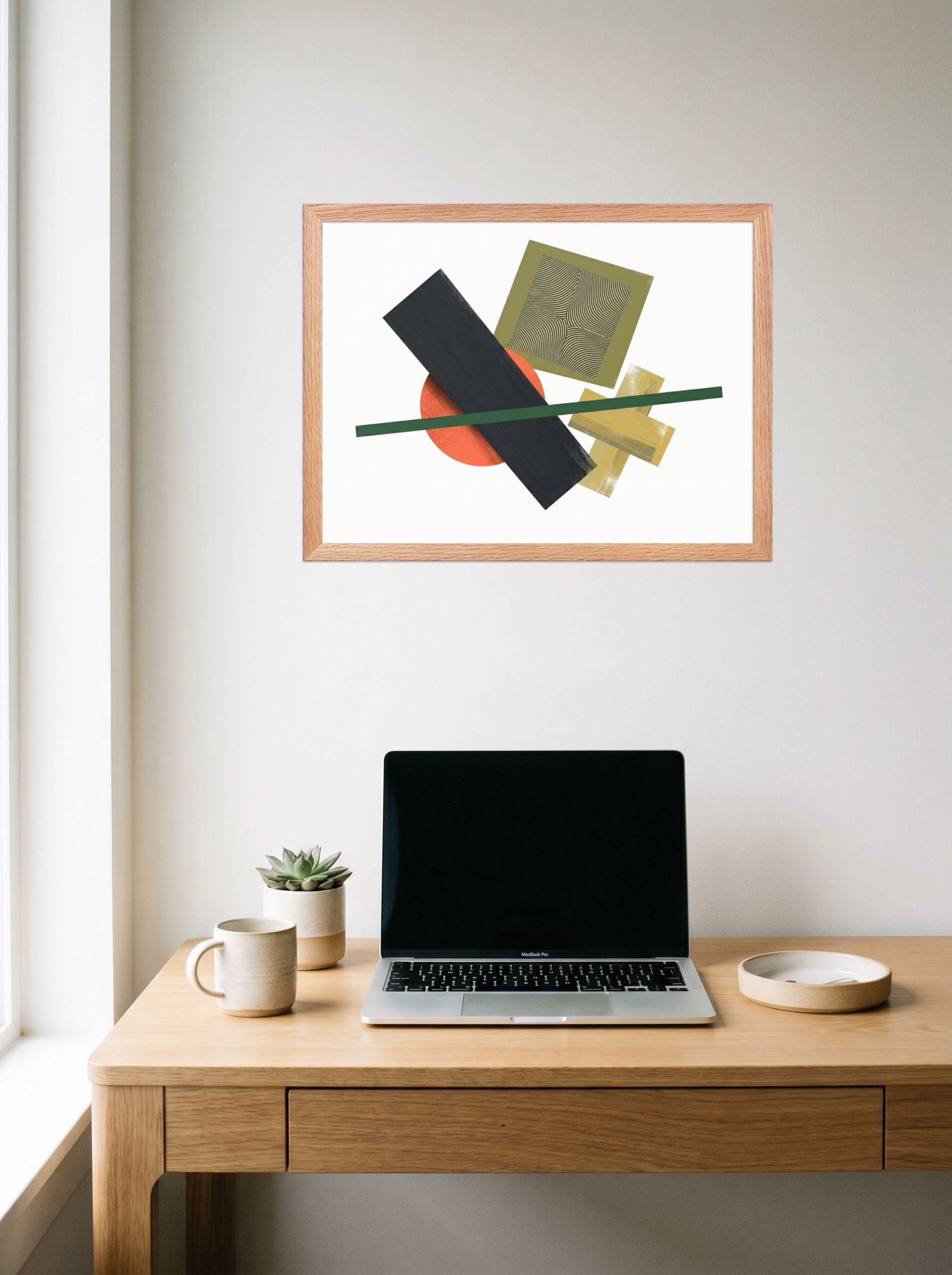 A 24x18 inch redoak framed Suprematism print of 'The Geometry of Sound' hanging above a worktable with a laptop.