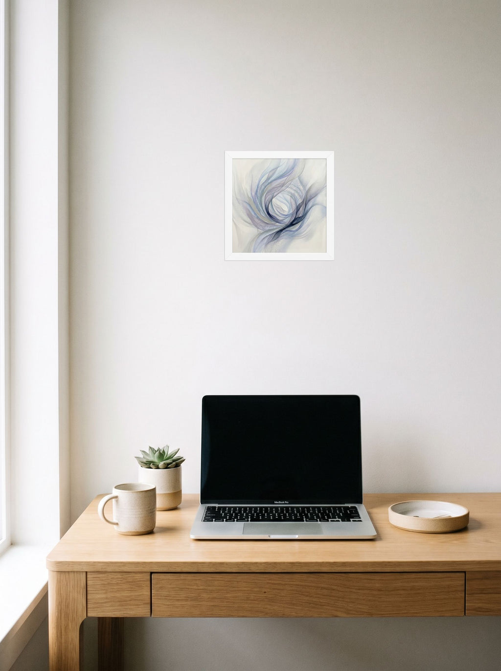 A 10x10 inch white framed Abstract art print of 'Ethereal Whispers in the Vortex' hanging above a worktable with a laptop.