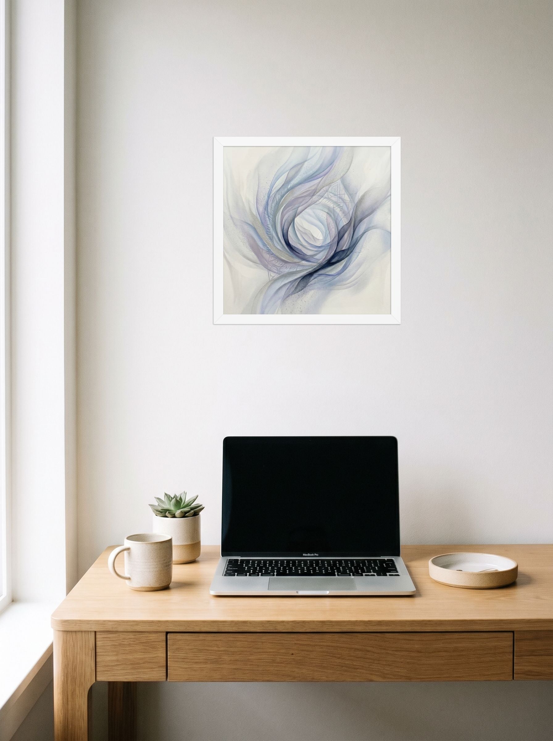 A 14x14 inch white framed Abstract art print of 'Ethereal Whispers in the Vortex' hanging above a worktable with a laptop.