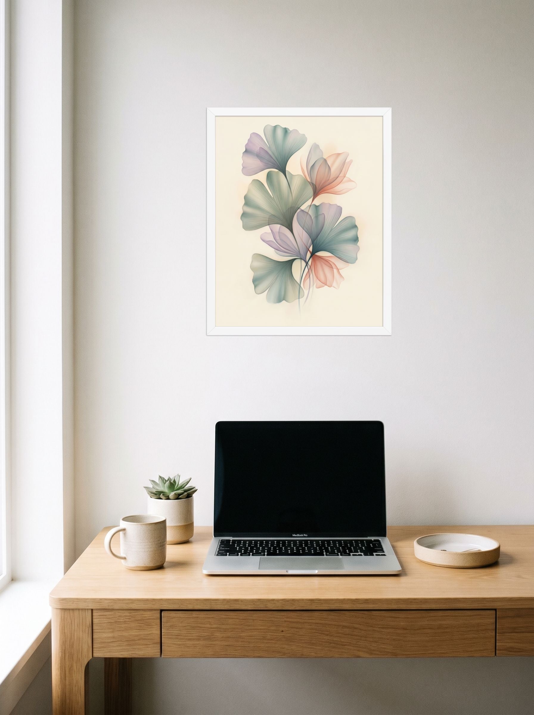 A 16x20 inch white framed Abstract art print of 'Ethereal Ginkgo Whispers' hanging above a worktable with a laptop.