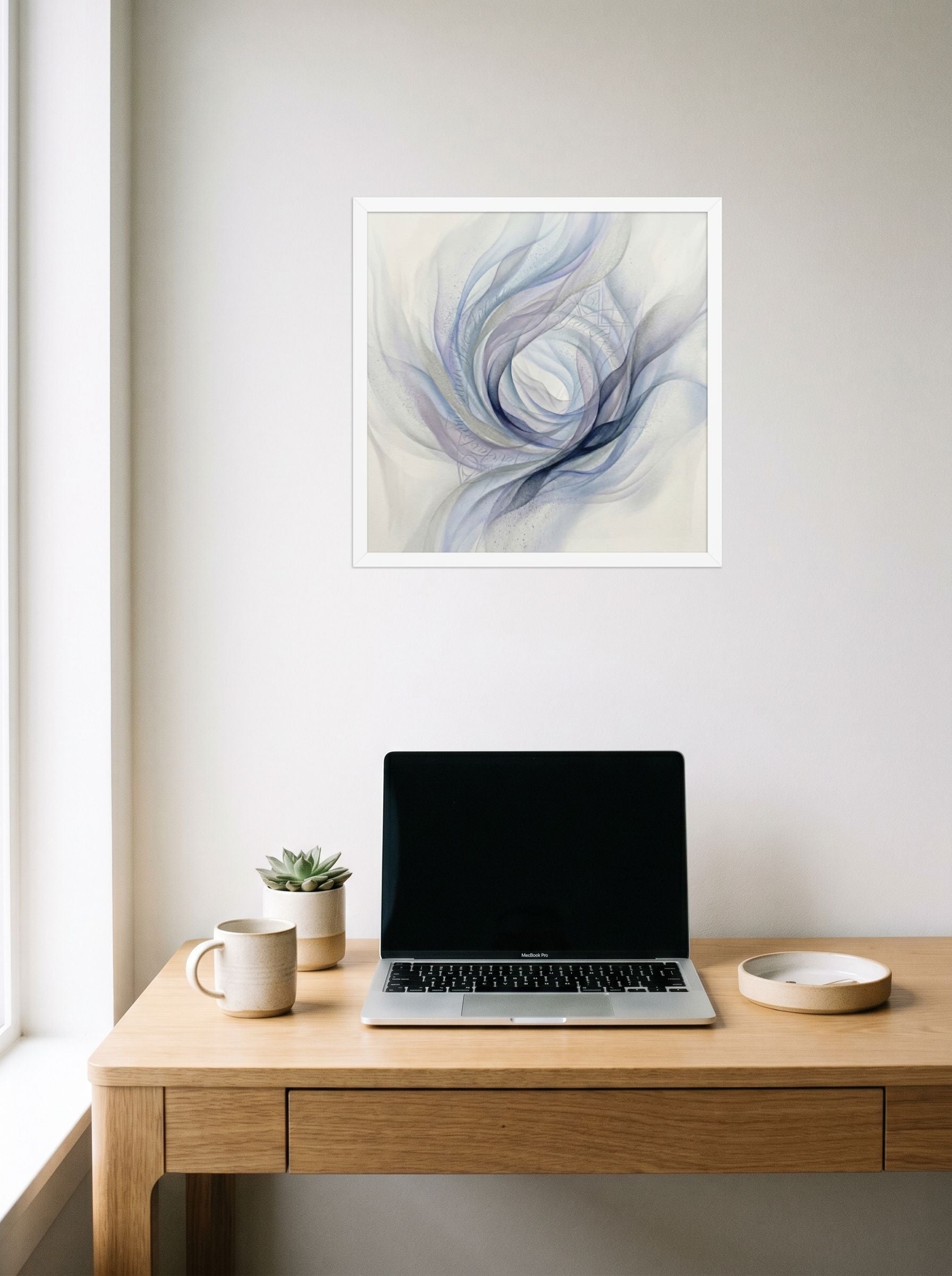 A 18x18 inch white framed Abstract art print of 'Ethereal Whispers in the Vortex' hanging above a worktable with a laptop.