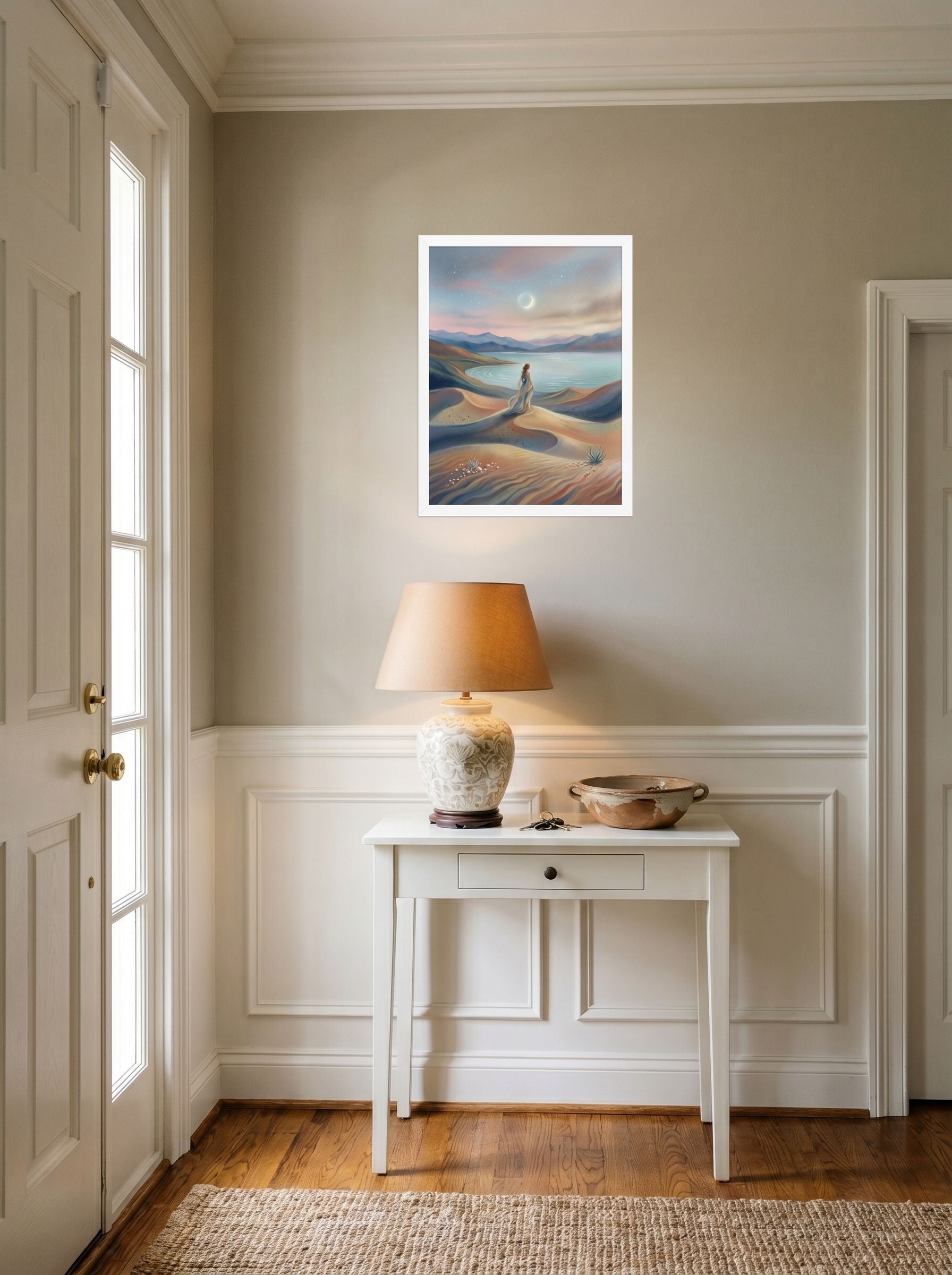A 18x24 inch white framed Magic realism print of 'Desert Moonrise' hanging in an entryway near a console.