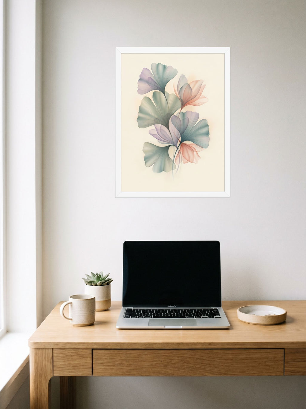 A 18x24 inch white framed Abstract art print of 'Ethereal Ginkgo Whispers' hanging above a worktable with a laptop.