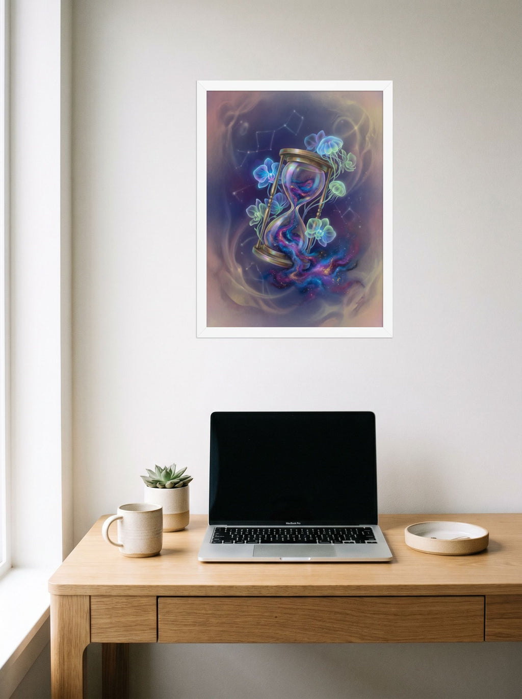 A 18x24 inch white framed Magic realism print of 'Sands of the Nebula' hanging above a worktable with a laptop.