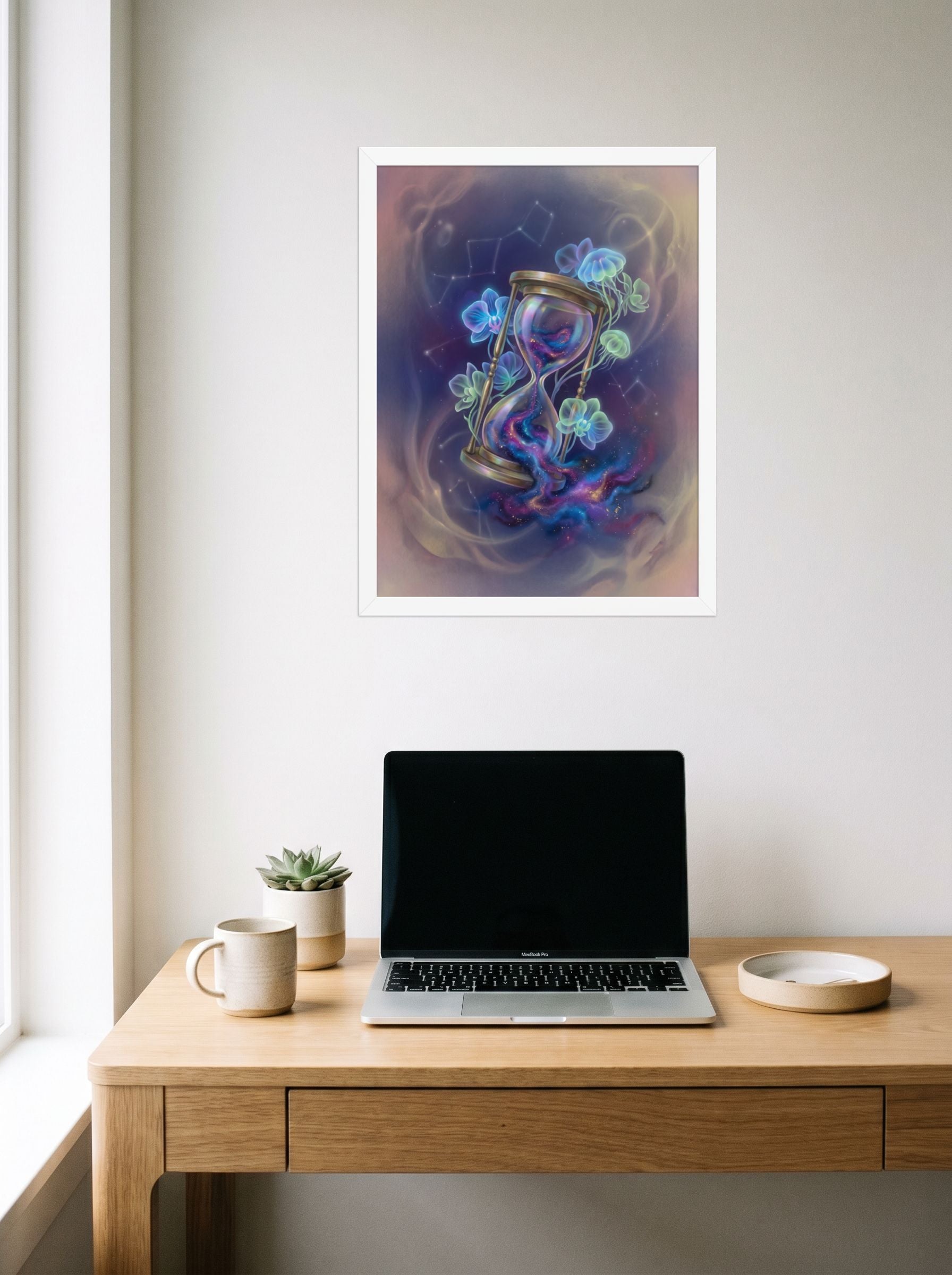 A 18x24 inch white framed Magic realism print of 'Sands of the Nebula' hanging above a worktable with a laptop.