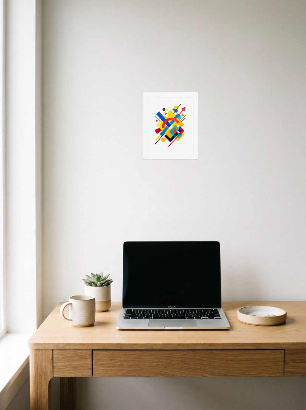 A 8x10 inch white framed Suprematism print of 'Directional Energy' hanging above a worktable with a laptop.