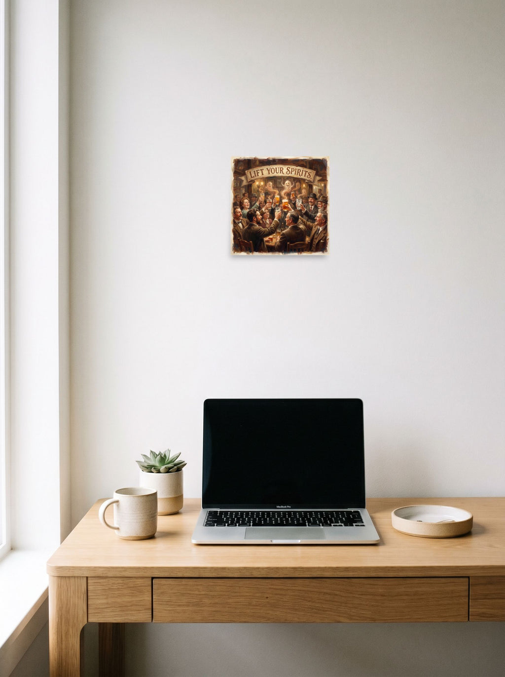 10x10 inch unframed paper print of 'Lift Your Spirits', hanging above a worktable with a laptop.