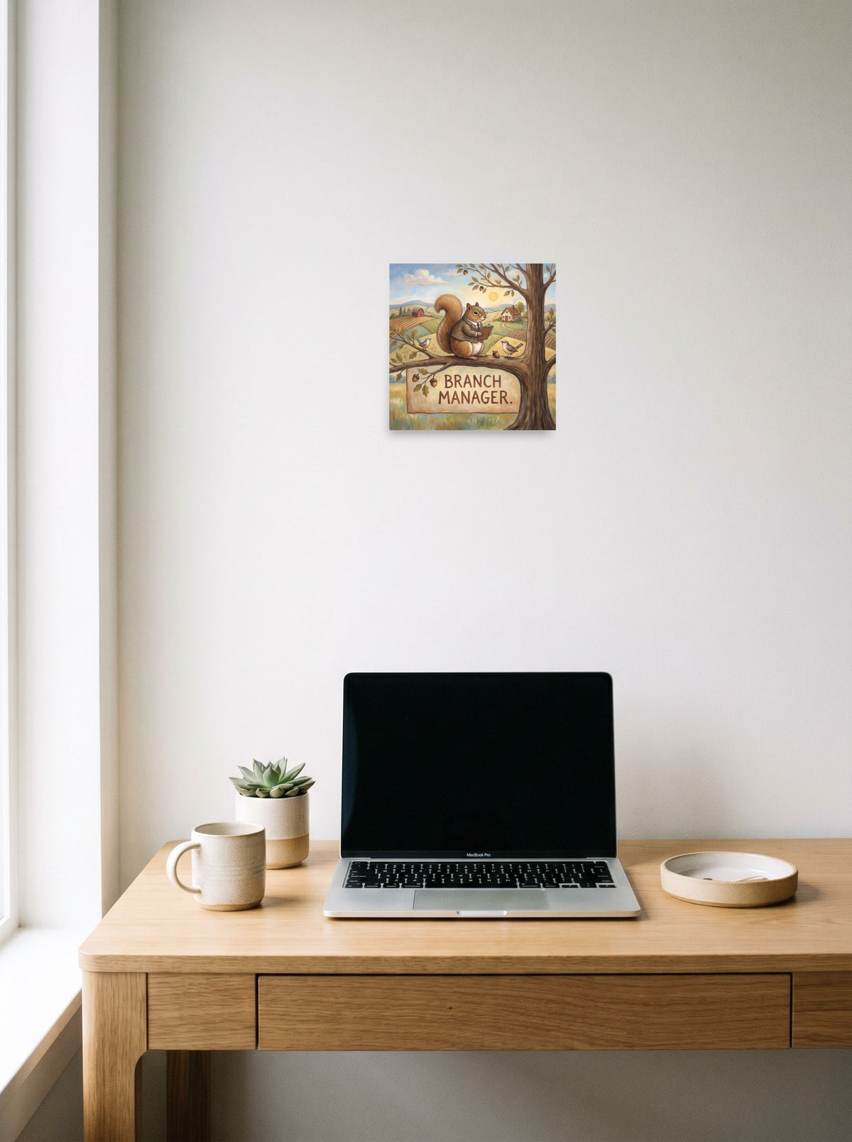 Folk art wall art 'Branch Manager', unframed paper at 10x10 inch, hanging above a worktable with a laptop.