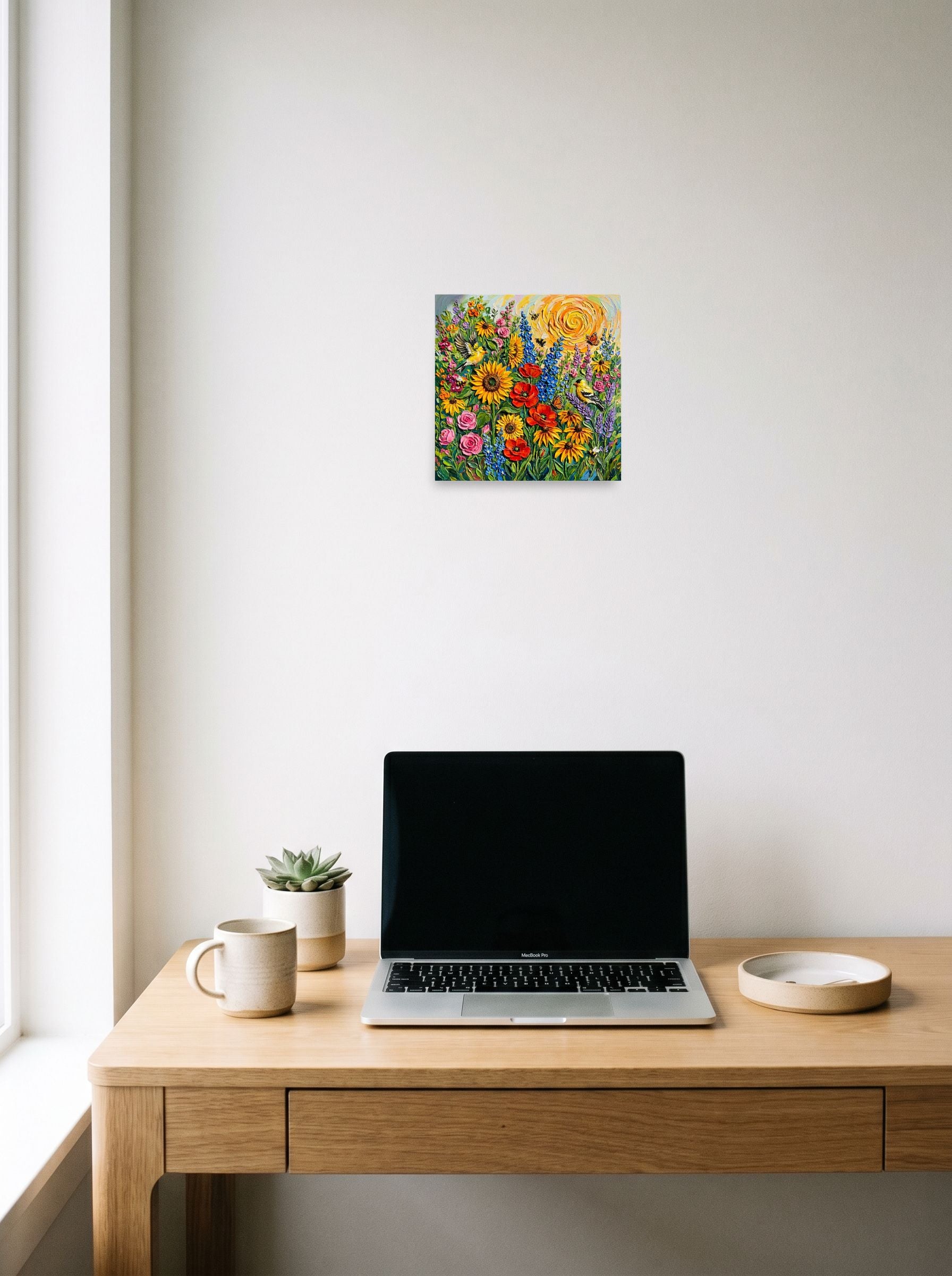 A 10x10 inch unframed paper Expressionism print of 'Sunburst Symphony' hanging above a worktable with a laptop.