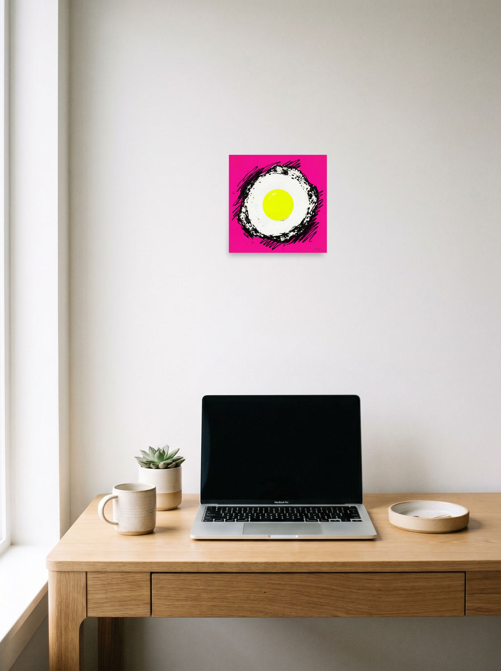 A 10x10 inch unframed paper Pop art print of 'Sunny Side Pop' hanging above a worktable with a laptop.
