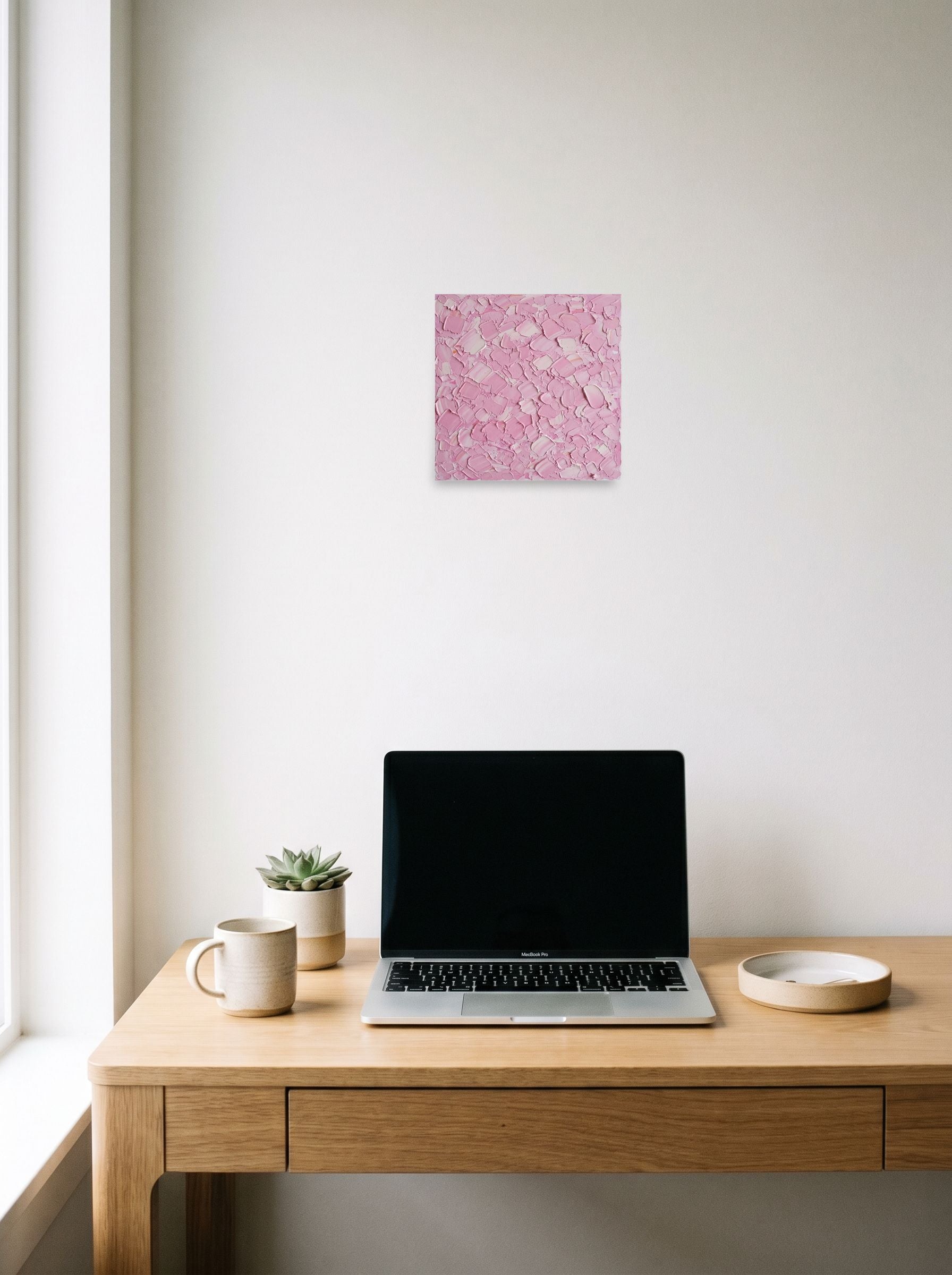 A 10x10 inch unframed paper Expressionism print of 'Blush Topography' hanging above a worktable with a laptop.