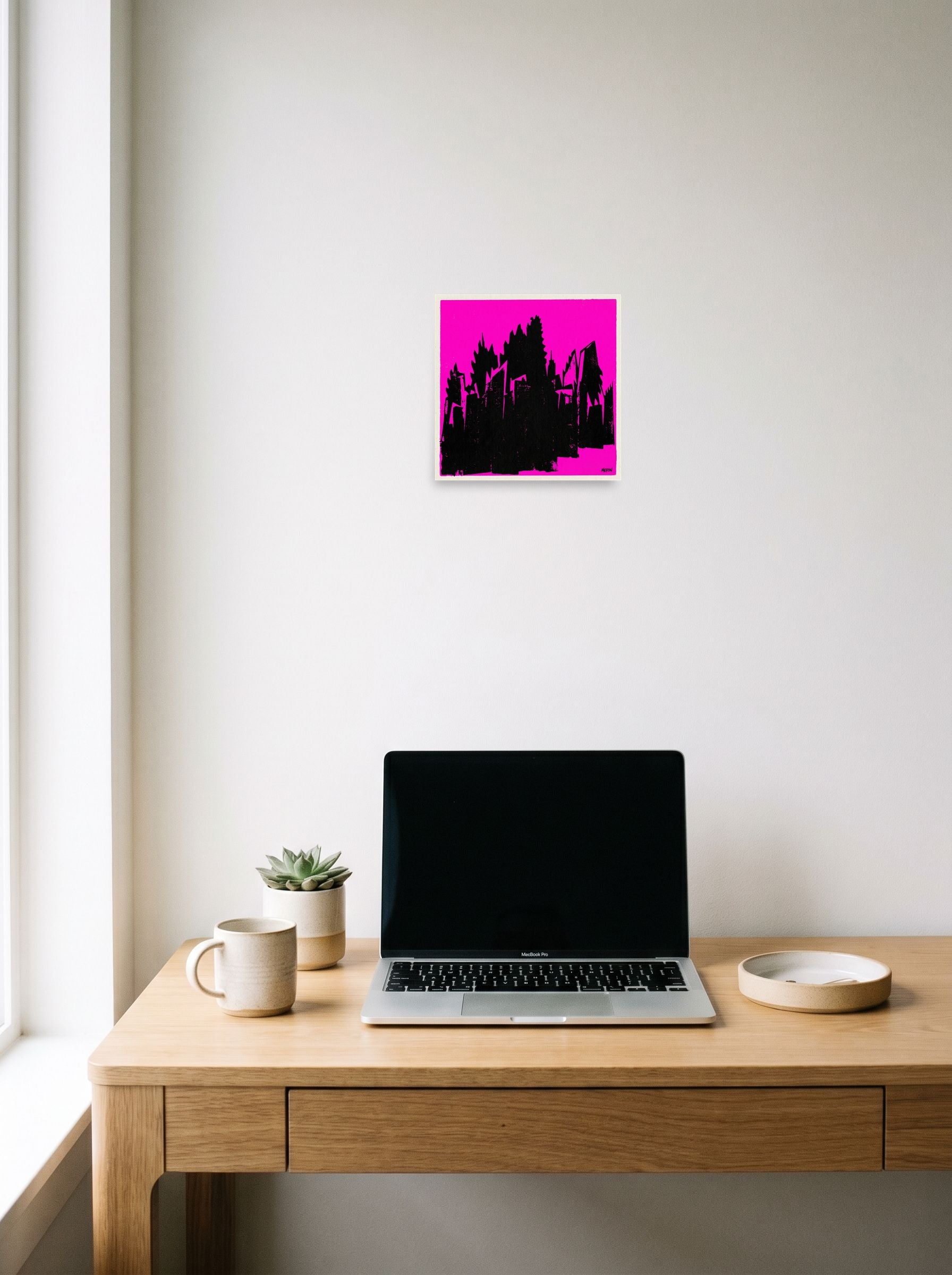 A 10x10 inch unframed paper Pop art print of 'Neon Urban Decay' hanging above a worktable with a laptop.