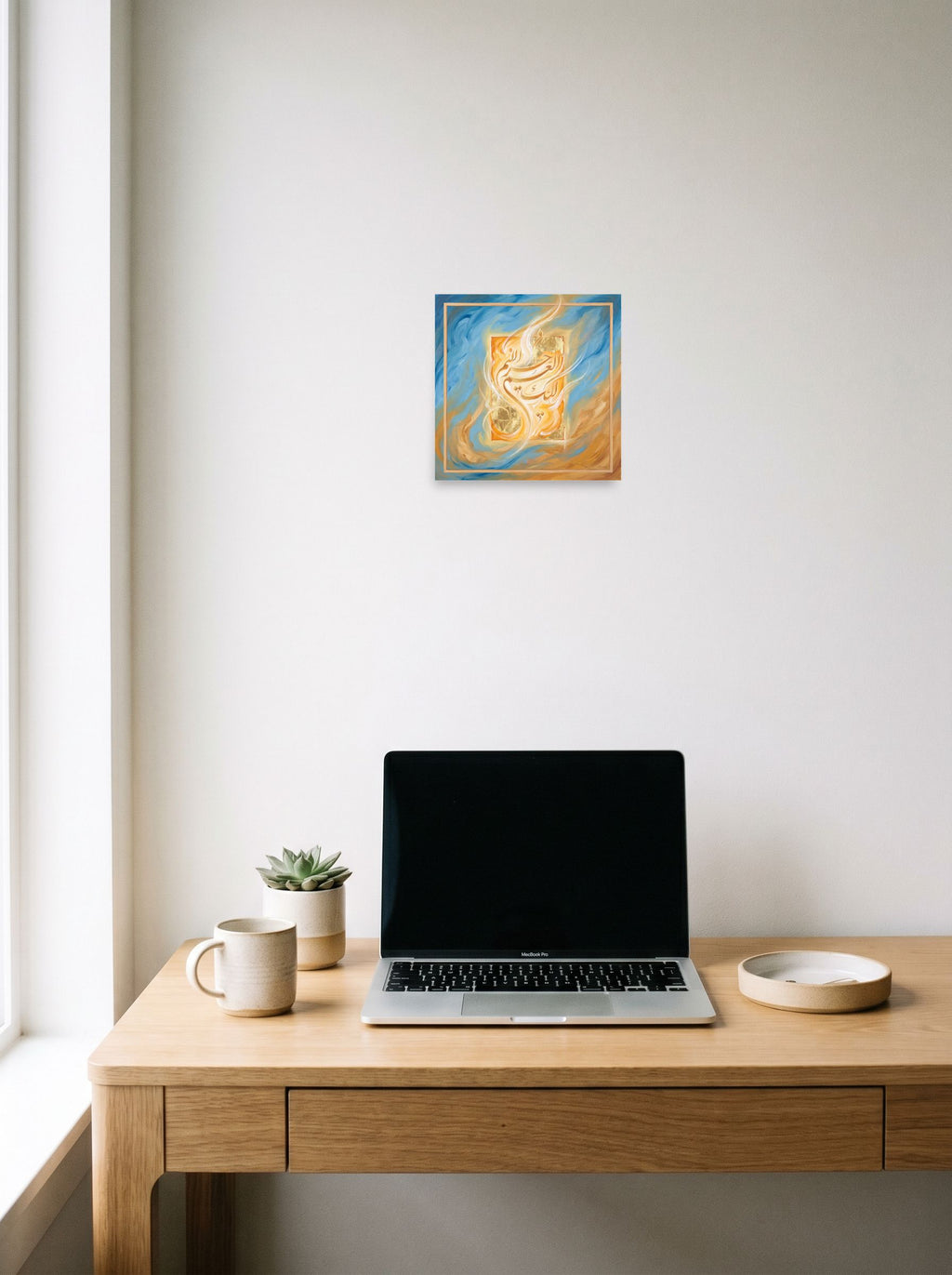 A 10x10 inch unframed paper Hurufiyya print of 'Luminous Script', hanging above a worktable with a laptop.