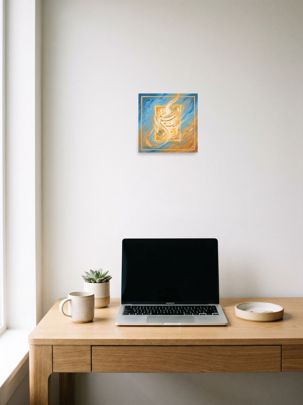A 10x10 inch unframed paper Hurufiyya print of 'Luminous Script', hanging above a worktable with a laptop.