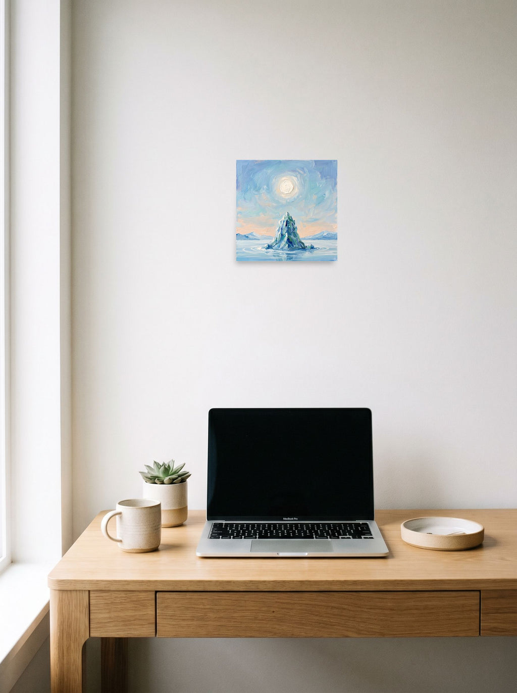 A 10x10 inch unframed paper Impressionism print of 'Frozen Peak' hanging above a worktable with a laptop.