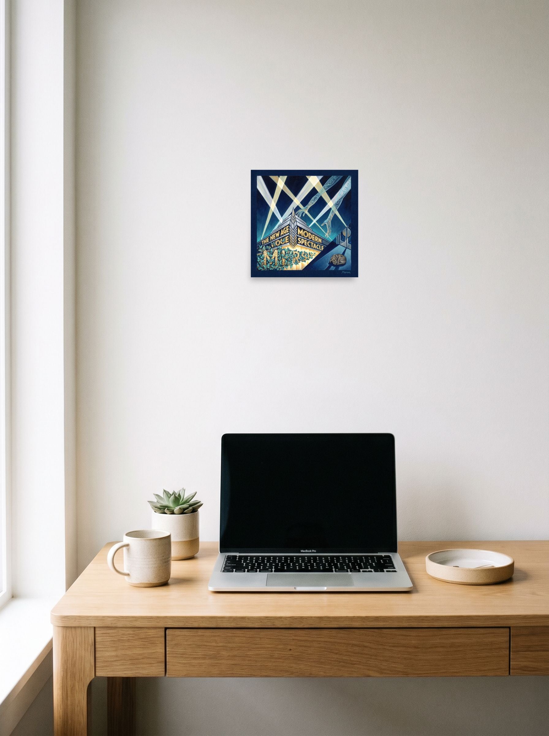 A 10x10 inch unframed paper Art Deco print of 'The New Age Spectacle' hanging above a worktable with a laptop.
