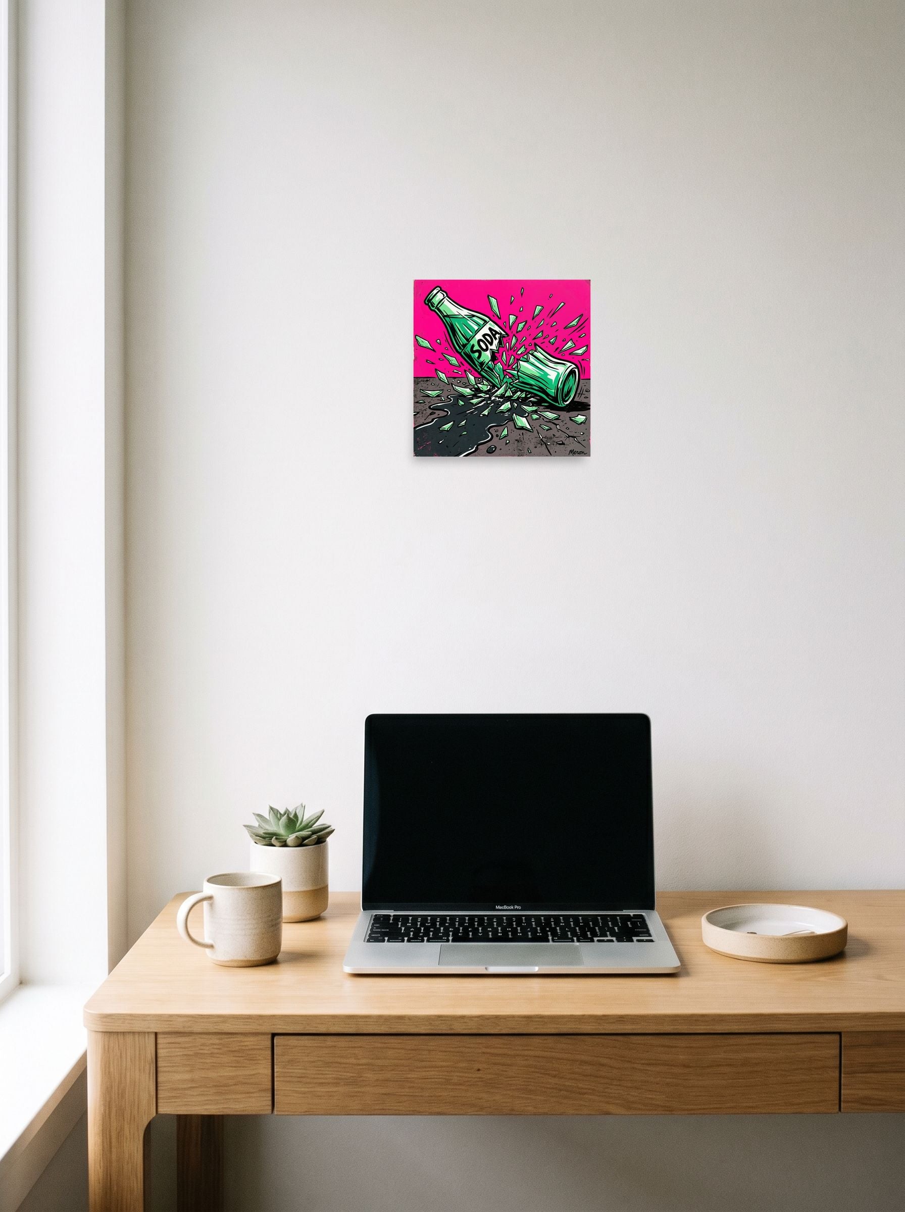 A 10x10 inch unframed paper Pop art print of 'Shattered Soda' hanging above a worktable with a laptop.
