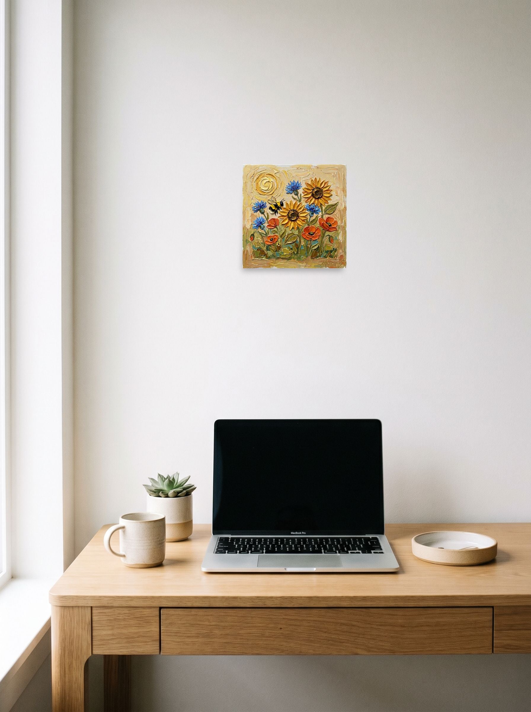 A 10x10 inch unframed paper Expressionism print of 'The Pollinator's Dance' hanging above a worktable with a laptop.