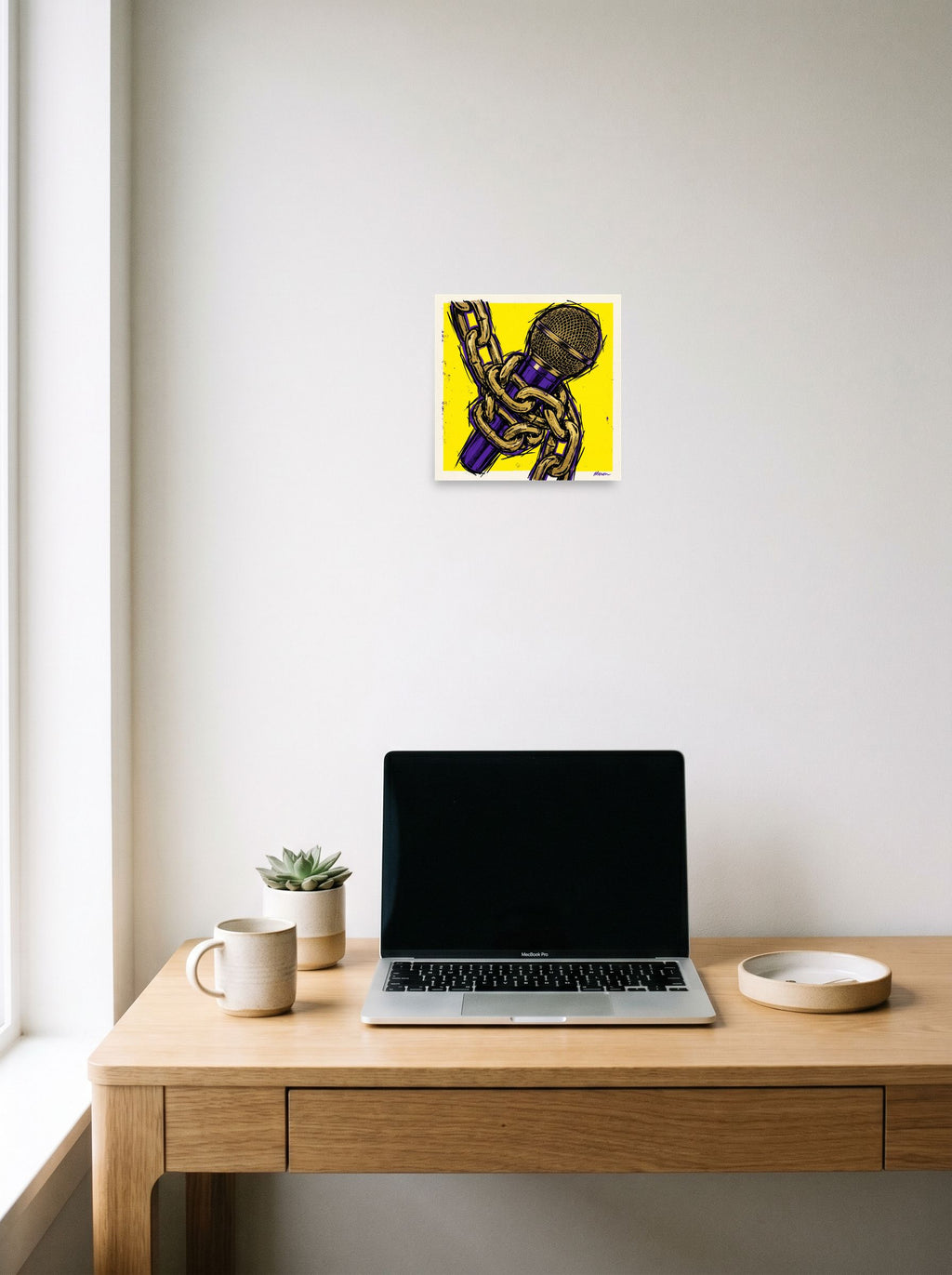 A 10x10 inch unframed paper Pop art print of 'Chained Mic' hanging above a worktable with a laptop.