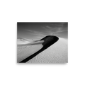 'Footsteps in the Void' — a Art photography print. A minimalist black and white photograph of sweeping sand dunes with a tiny figure walking along the ridge, perfect for adding a sense of scale to an Office.