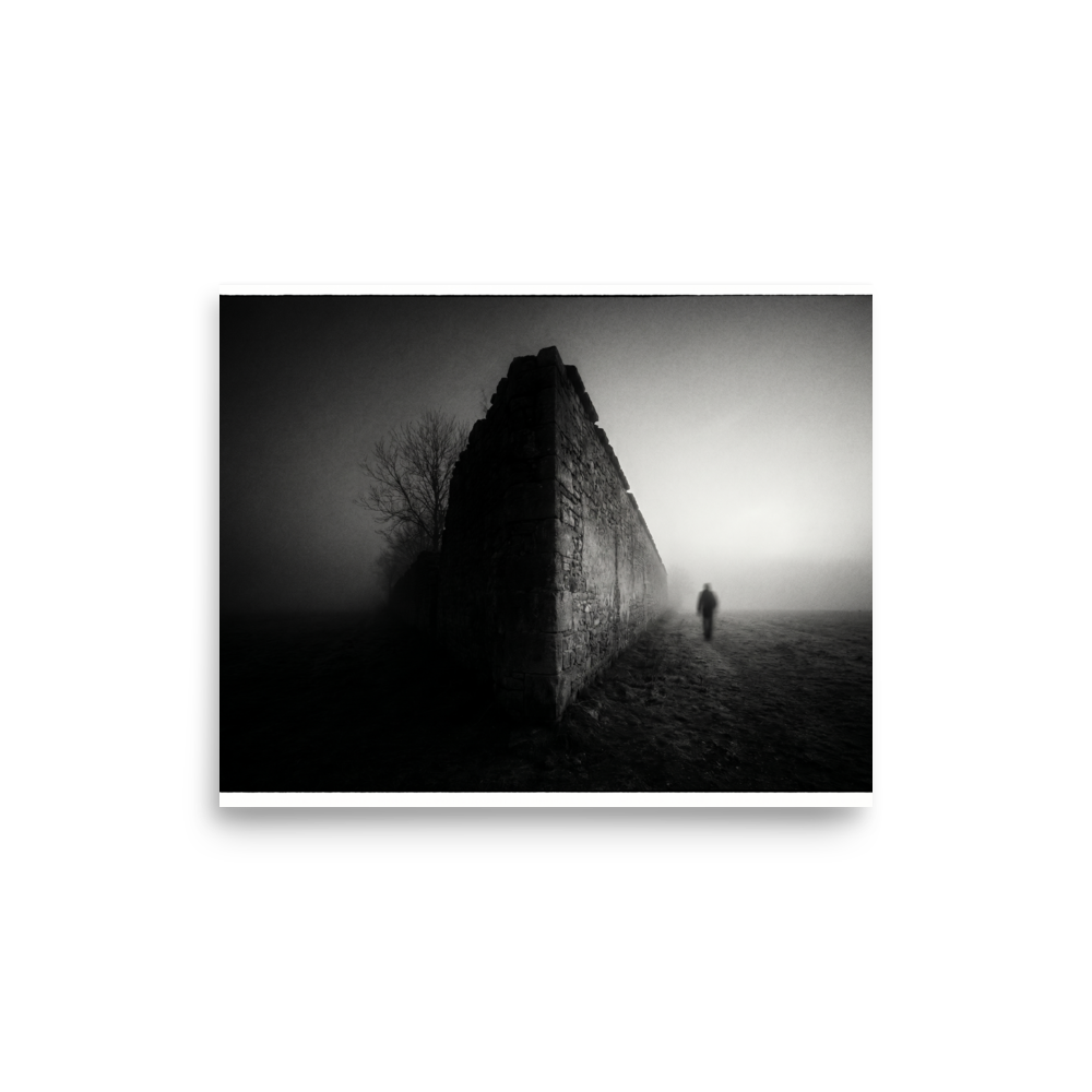 'Echoes in the Mist' — a Art photography print. A moody black and white photograph of a lone figure walking into dense fog next to an old stone wall, ideal for a modern Office or Den.