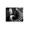 'Descent into Light' — a Art photography print. A high-contrast black and white photograph looking down a spiral stone staircase illuminated by a small window, adding depth and intrigue to an Office or Hallway.