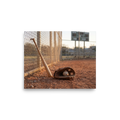 'Field of Memories' — a Art photography print. A photograph of a baseball bat leaning against a fence next to a glove and ball on a dirt field at sunset, a nostalgic piece for a Game Room.