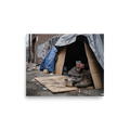 'Urban Realities' — a Art photography print. A photograph of a makeshift shelter made of tarps and cardboard on a dirty city street, with a person sitting inside holding a cup, a striking piece for a Gallery.