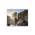 'Steps Through Time' — a Art photography print. Creative puddle reflection photograph showing a work boot and a dress shoe on cobblestones, with a modern glass skyscraper and an old stone building in the background, ideal for an office or hallway.